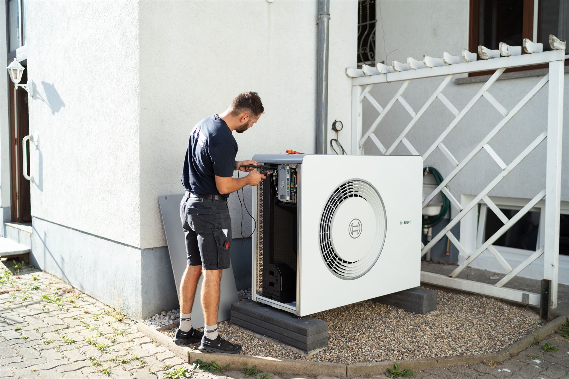 Techniker arbeitet an der geöffneten Außeneinheit einer Wärmepumpe mit sichtbarer Elektronik